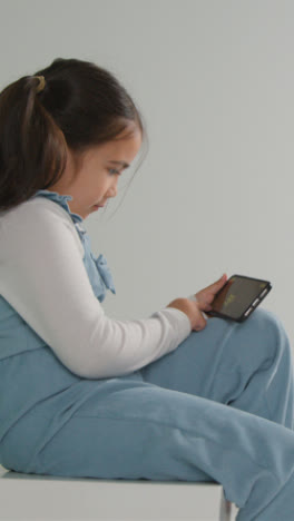 Vertical-Video-Studio-Shot-Of-Young-Girl-On-ASD-Spectrum-Gaming-On-Mobile-Phone-Against-White-Background-2